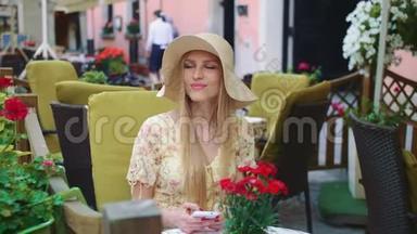 在外面餐馆里微笑的女人。 在舒适的街道上，坐在外面餐馆里的一位开朗的年轻女人。